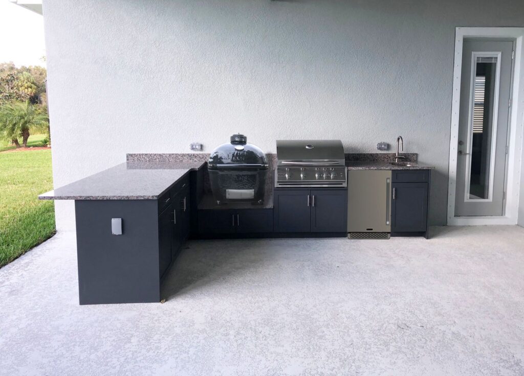 L shaped outdoor kitchen with grey granite countertops and dark grey cabinets featuring a gas grill and a "Big Green Egg" kamado grill