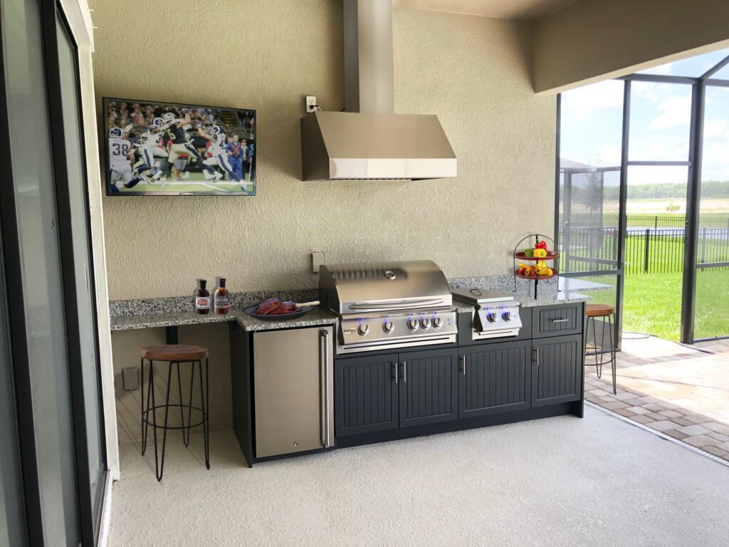 Custom outdoor kitchen with a mounted TV and custom vent hood above grill by Synergy Outdoor Living 