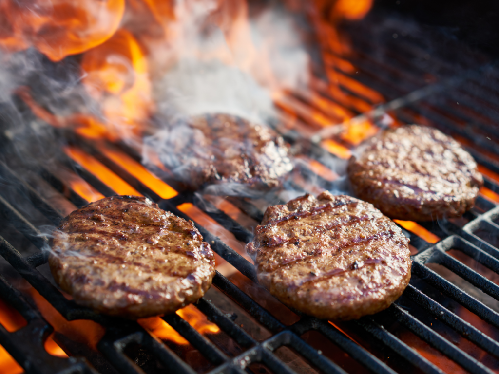 Burgers grilling on a grill with smoke and flames 