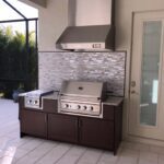 brown outdoor kitchen with vent hood and grill with beautiful backsplash