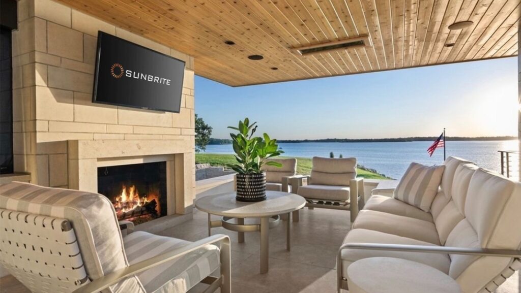 Outdoor seating area in a waterfront backyard with a Sunbrite tv mounted above the fireplace