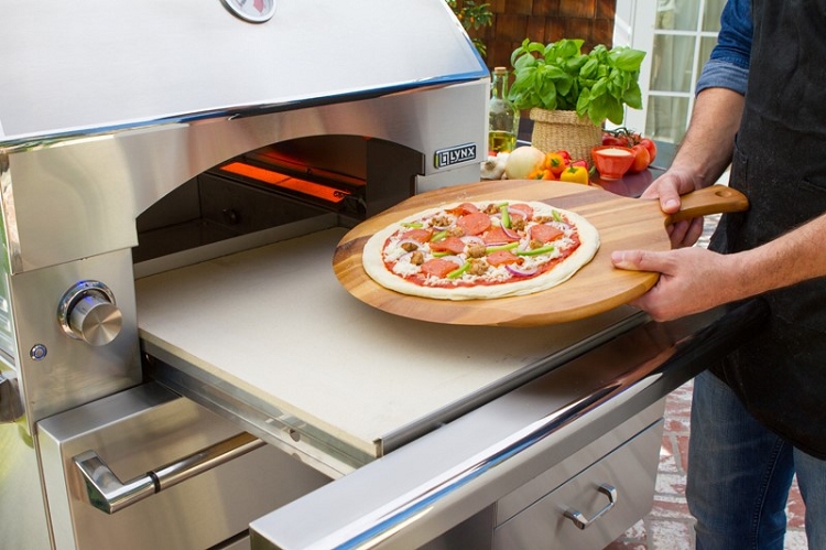 man putting pizza inside of outdoor pizza oven 