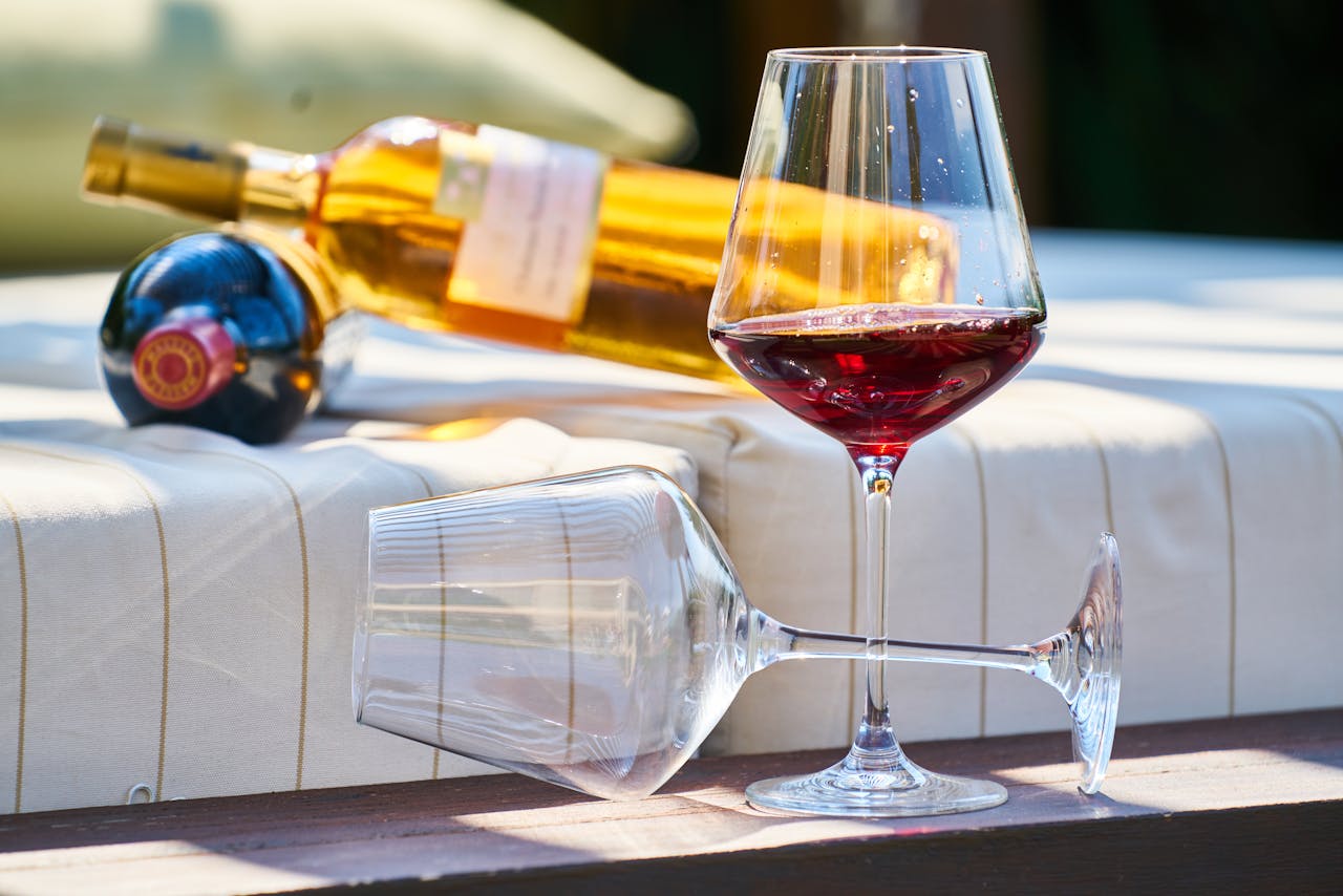 wine glasses sitting outside with red wine and bottles of wine behind